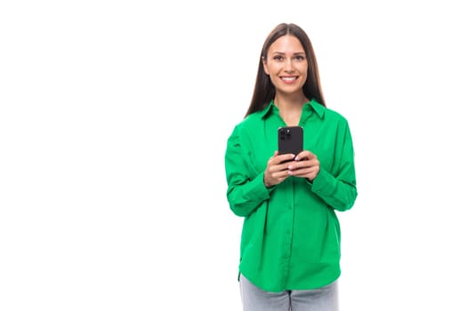 cute young European brown-eyed female model with well-groomed black hair and make-up dressed in a green shirt with a phone in her hands.