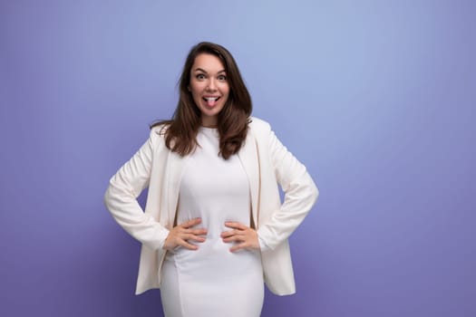 cheerful brunette woman in ivory jacket and white dress posing in studio.