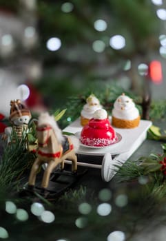 Christmas still life with a cake in the form of a red Santa's hat on a sleigh on a background of a wooden horse with bokeh. High quality photo