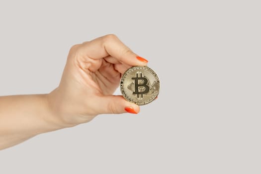 Closeup of woman hand showing golden bitcoin, cryptocurrency, virtual money. Indoor studio shot isolated on gray background.