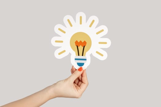 Closeup of woman hand showing paper bulb, symbol of creative idea and inspiration. Indoor studio shot isolated on gray background.