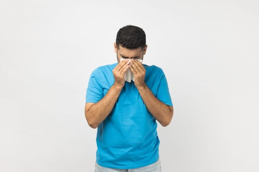 Portrait of stressed offended unshaven man wearing blue T- shirt standing with hand down and crying, expressing sorrow and sadness. Indoor studio shot isolated on gray background.