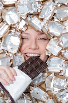 The face of a Caucasian woman surrounded by candy wrappers. The girl eats a bar of chocolate