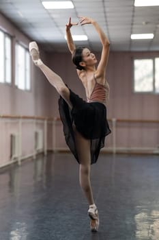 Graceful Asian ballerina in a beige bodysuit and black skirt is rehearsing in a dance class