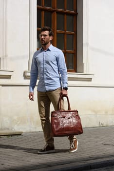 Handsome businessman walking on the street, with luxury leather briefcase. Fashionable style. Street photo