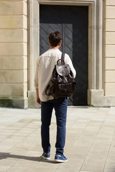 Handsome businessman walking on the street, with luxury leather backpack. Man wearing blue pants, sneakers, white t-shirt and beige shirt