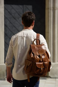 Handsome businessman walking on the street, with luxury leather backpack. Man wearing blue pants, sneakers, white t-shirt and beige shirt
