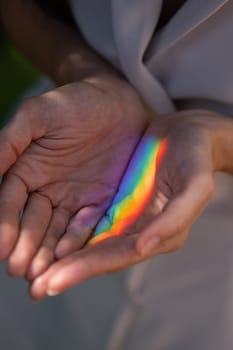 Faceless woman catching rainbow ray with her hands outdoors