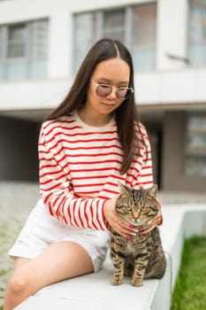 Young woman and tabby cat sitting on a bench outdoors