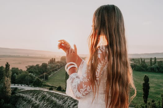 Romantic beautiful bride in white dress posing with sea and mountains in background. Stylish bride standing back on beautiful landscape of sea and mountains on sunset