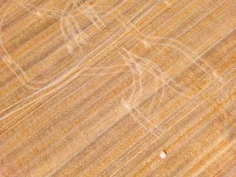 Striking tracks and patterns from a tractor on a dry agricultural field with straw bales, aerial view from Germany
