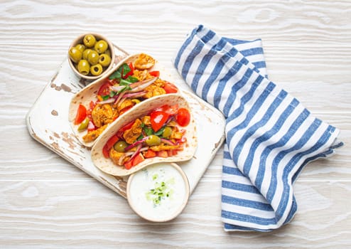 Traditional Greek Dish Gyros: Pita bread Wraps with vegetables, meat, herbs, olives on rustic wooden cutting board with Tzatziki sauce, olive oil top view, white wooden summer background.