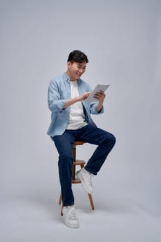 Happy young man sitting on chair and using tablet over grey background
Happy young man sitting on chair and using tablet over grey background

