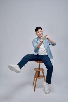 Young man using smartphone, chatting online, browsing social media, sitting on chair 