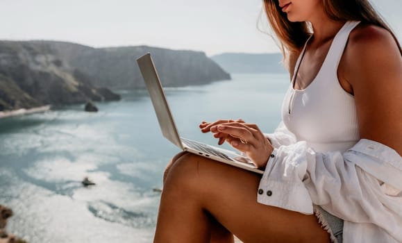 Digital nomad, Business woman working on laptop by the sea. Pretty lady typing on computer by the sea at sunset, makes a business transaction online from a distance. Freelance remote work on vacation