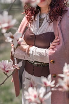 Magnolia park woman. Stylish woman stands near the magnolia bush in the park. Dressed in white corset pants and posing for the camera