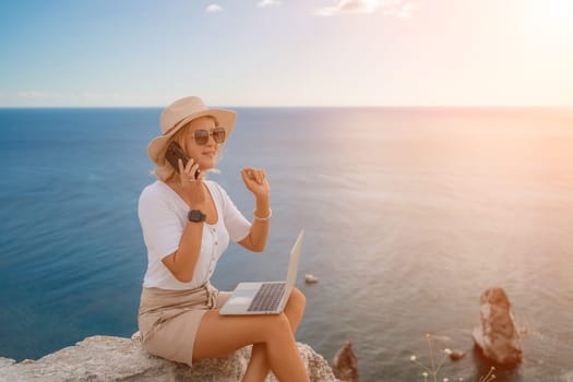 Freelance women sea. She is working on the computer, talking on the phone in the open air with a beautiful view of the sea. The concept of remote work