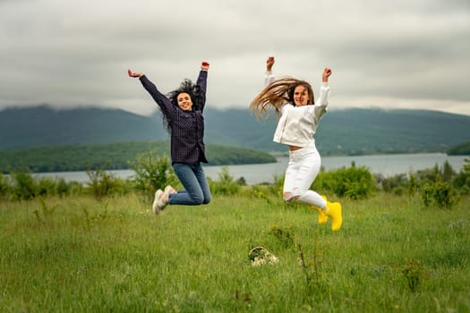 Two girls with long hair are jumping in a clearing overlooking the mountains. The concept of travel and tourism to different countries