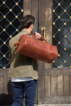 a man with a bag. black leather travel bag, street photo. man is wearing blue sneakers, jeans, a white T-shirt and a jacket.