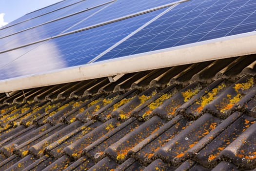 Yellow and orange stains on brown roof tiles underneath solar panels on house roof, Germany