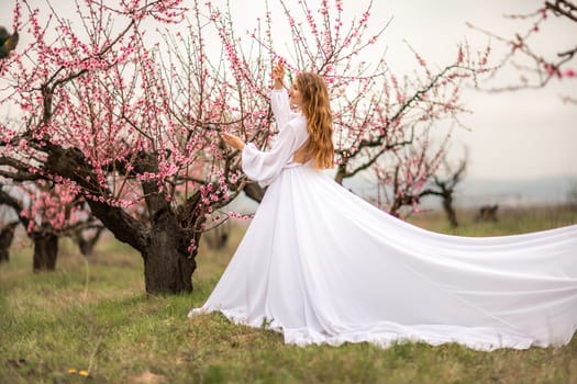 Woman peach blossom. Happy curly woman in white dress walking in the garden of blossoming peach trees in spring.