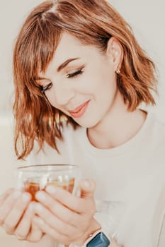 Woman drinks tea close-up. Portrait of a brunette in a white T-shirt with a transparent mug in her hands