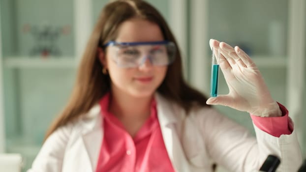 Scientist student woman looks at blue solution and test tube working in equipped laboratory. Toxic poisonous liquid in lab