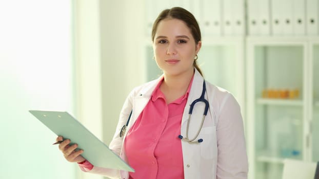 Portrait of happy confident female doctor posing with clipboard and looking at camera. Doctor is happy with possibility of counseling and access to medical records and test results