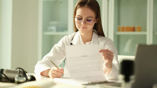 Female doctor makes entries in journal and medical practitioner fills out medical paperwork. Cardiologist examining patient form medical history or prescription