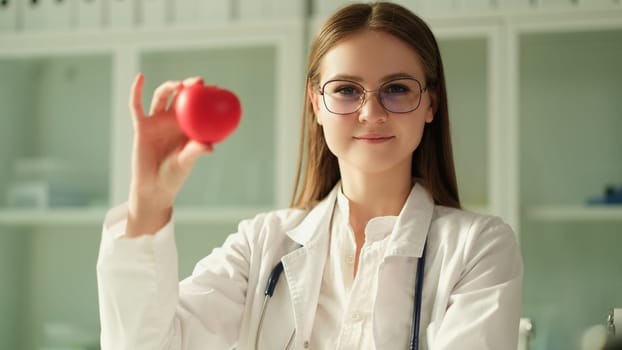 Happy female cardiologist doctor holding heart figure in hands. Nurse or therapist reminding about regular procedures for examining patients