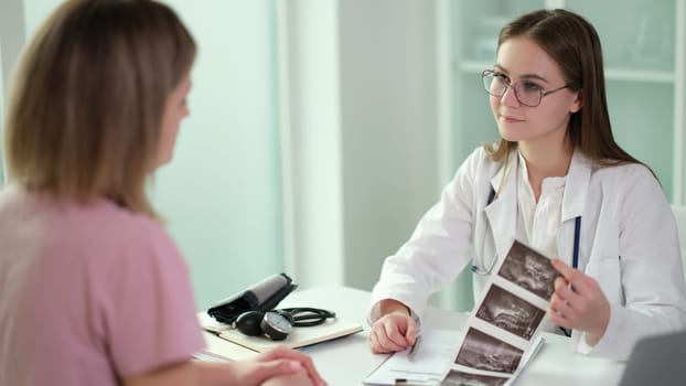 Gynecologist doctor communicates with patient and examines results of ultrasound examination of internal organs in clinic. Examination and X-ray of fetus