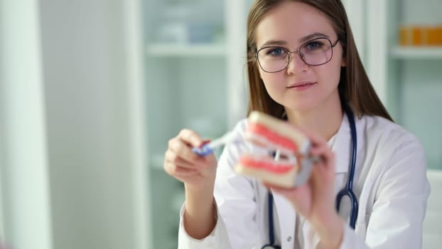 Woman dentist holds model of jaws and toothbrush in hands. Dentist shows how to brush teeth correctly