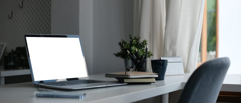 Laptop with blank display, coffee cup and stationery on white office desk.