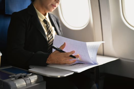 Beautiful middle age businesswoman working with document in aircraft during business travel.