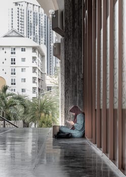 Bangkok, Thailand - Jul 28, 2023 - Portrait of Muslim lady is resting and using her smartphone while sitting on the floor. Religious islamic woman in hijab enjoying playing social networks, Space for text, Selective focus.