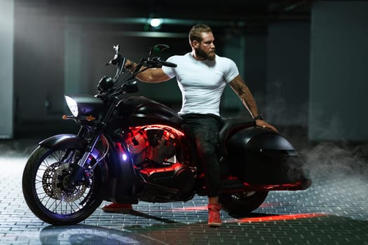Sexy handsome attractive sporty muscular fitness model breaded biker in white tight tshirt sits on brutal beautiful motorcycle in the parking