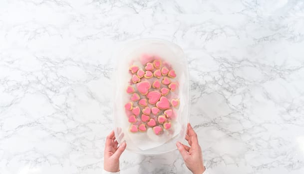 Flat lay. Storing heart-shaped sugar cookies with pink and white royal icing in a large plastic container.