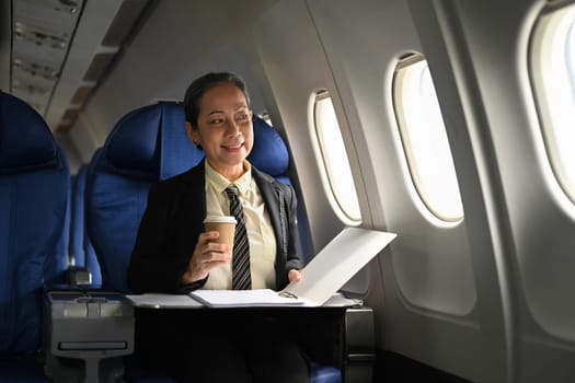 Beautiful middle age businesswoman working with document in aircraft during business travel.