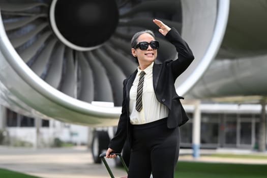 Elegant mature businesswoman walking near the airport with a suitcase. Business travel concept.