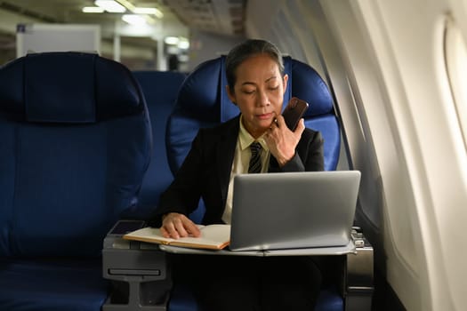 Beautiful middle age businesswoman working with document in aircraft during business travel.