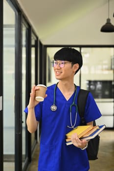 Portrait of medical student man wearing blue scrubs with stethoscope standing near window at campus.