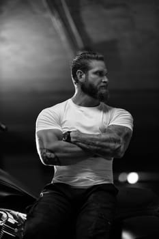 Sexy handsome attractive sporty muscular fitness model breaded biker in white tight tshirt sits on brutal beautiful motorcycle in the parking, black and white photo