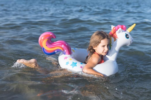 Happy baby girl swimming on an inflatable swimming unicorn in the sea.