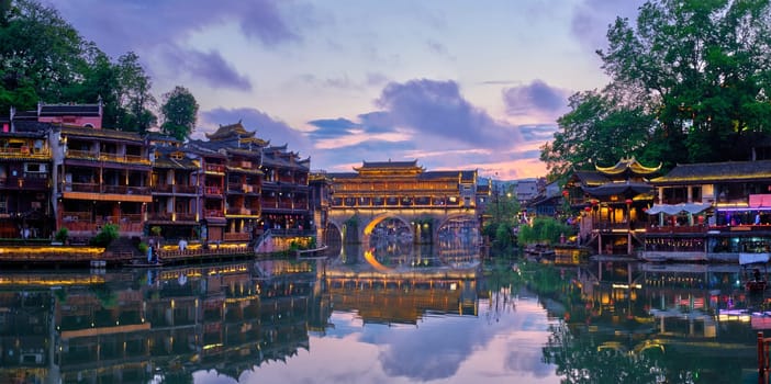 Chinese tourist attraction destination - panorama of Feng Huang Ancient Town (Phoenix Ancient Town) on Tuo Jiang River illuminated at night. Hunan Province, China