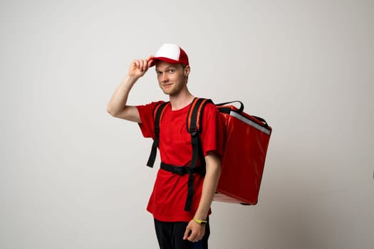 Young delivery guy employee man in red uniform work as courier and hold a red thermal food bag backpack isolated on white background studio. Food delivery dervice concept