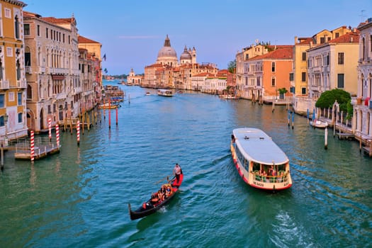 VENICE, ITALY - JULY 19, 2019: View of Venice Grand Canal with boats gondola and vaporetto and Santa Maria della Salute church in the day from Ponte dell'Accademia bridge on sunset. Venice, Italy