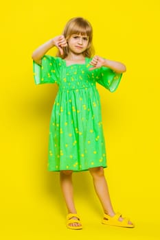 Dislike. Upset young preteen child girl kid showing thumbs down sign gesture, expressing discontent, disapproval, dissatisfied bad work indoors. Displeased cute children on yellow background. Vertical