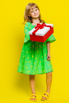 Lovely smiling young preteen child girl kid presenting birthday gift box stretches out hands, offer wrapped present career bonus, celebrating party. Little cute children on yellow background. Vertical