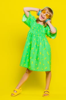 School girl listening music via headphones and dancing disco party fooling around having fun expressive gesticulating hands. Preteen Caucasian child kid in sunglasses on yellow background. Vertical