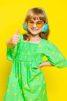 School girl listening music via headphones and dancing disco party fooling around having fun expressive gesticulating hands. Preteen Caucasian child kid in sunglasses on yellow background. Vertical